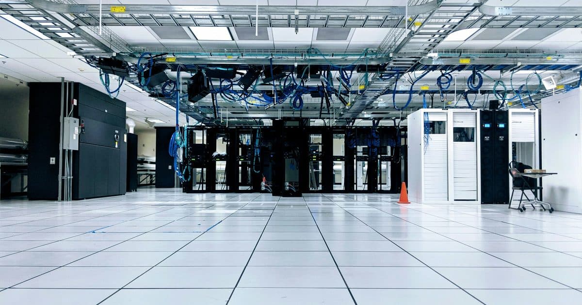 Wide view of a data center floor with server racks and overhead cabling